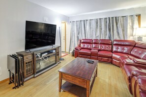 Una sala de estar con televisor de pantalla plana, una mesa de centro de madera y un sofá de cuero rojo.