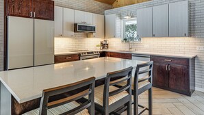 A kitchen with a large island, wooden cabinets, a microwave, and a clock on the wall. - Sauna & Game Room! Tranquil Retreat on Grace Lake (Watersmeet)