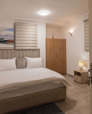 Een slaapkamer met een bed, een houten garderobe, een nachtkastje met een lamp, en een wandlamp.