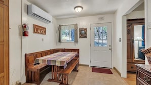 A dining area with a wooden table and benches, a fire extinguisher, a welcome sign, and a door with a view of the outdoors. - Lakefront Cabin w/ Dock, Kayaks & Full Kitchen (Nevada City)
