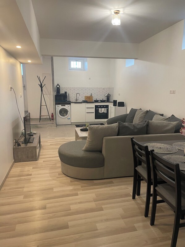 A modern living room with a curved sofa, a dining table with chairs, and a kitchen in the background.