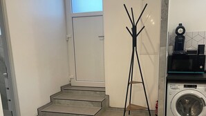 Ett utrymme för tvätt med en tvättmaskin, ett torkställ och en dörr som leder till ett annat rum.