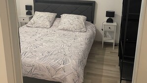 Ett sovrum med en säng, två sängbord, ett litet bord, en svart hyllsektion och en taklampa.