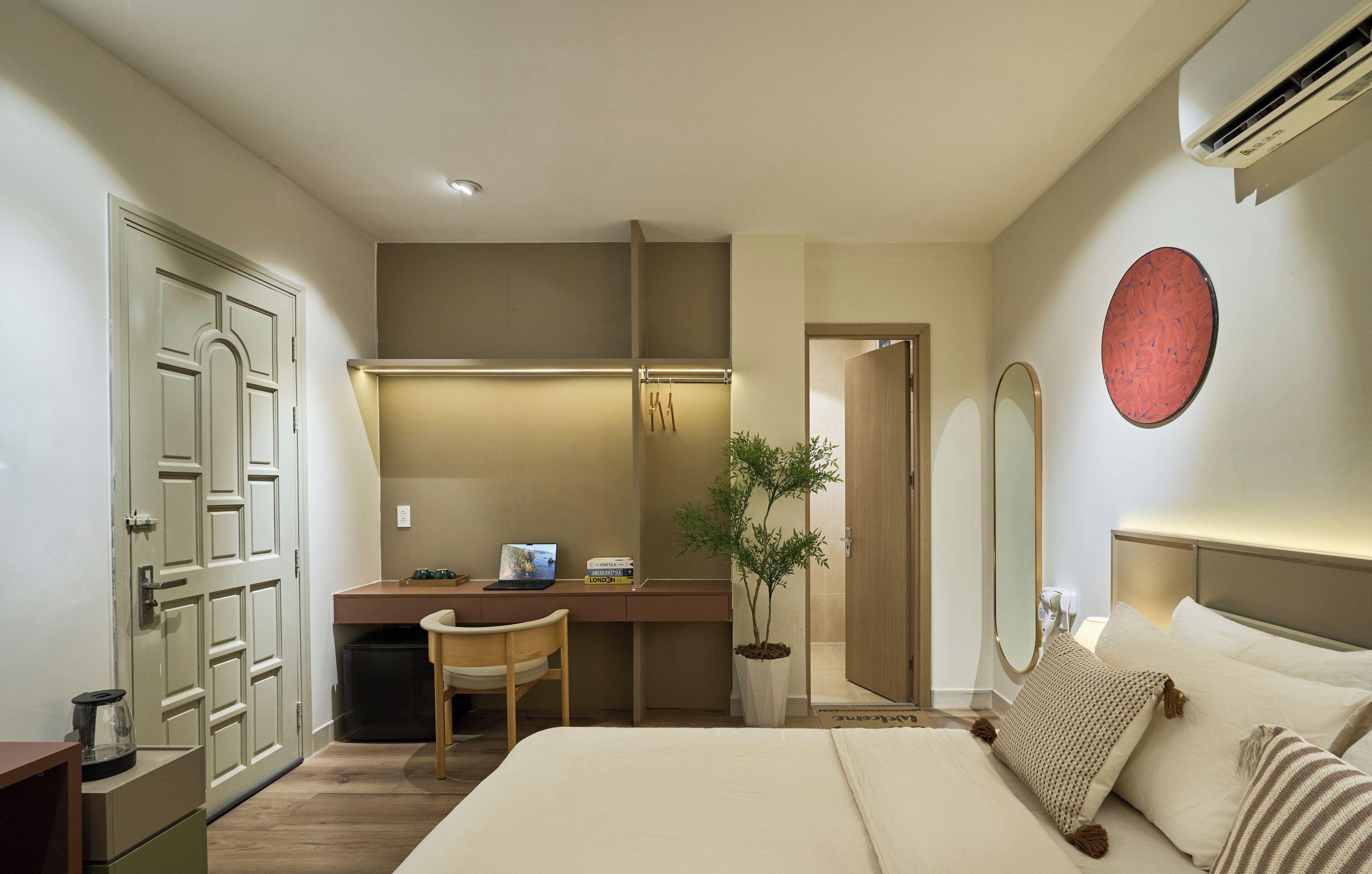 A hotel room with a bed, desk, chair, potted plant, and a large mirror.