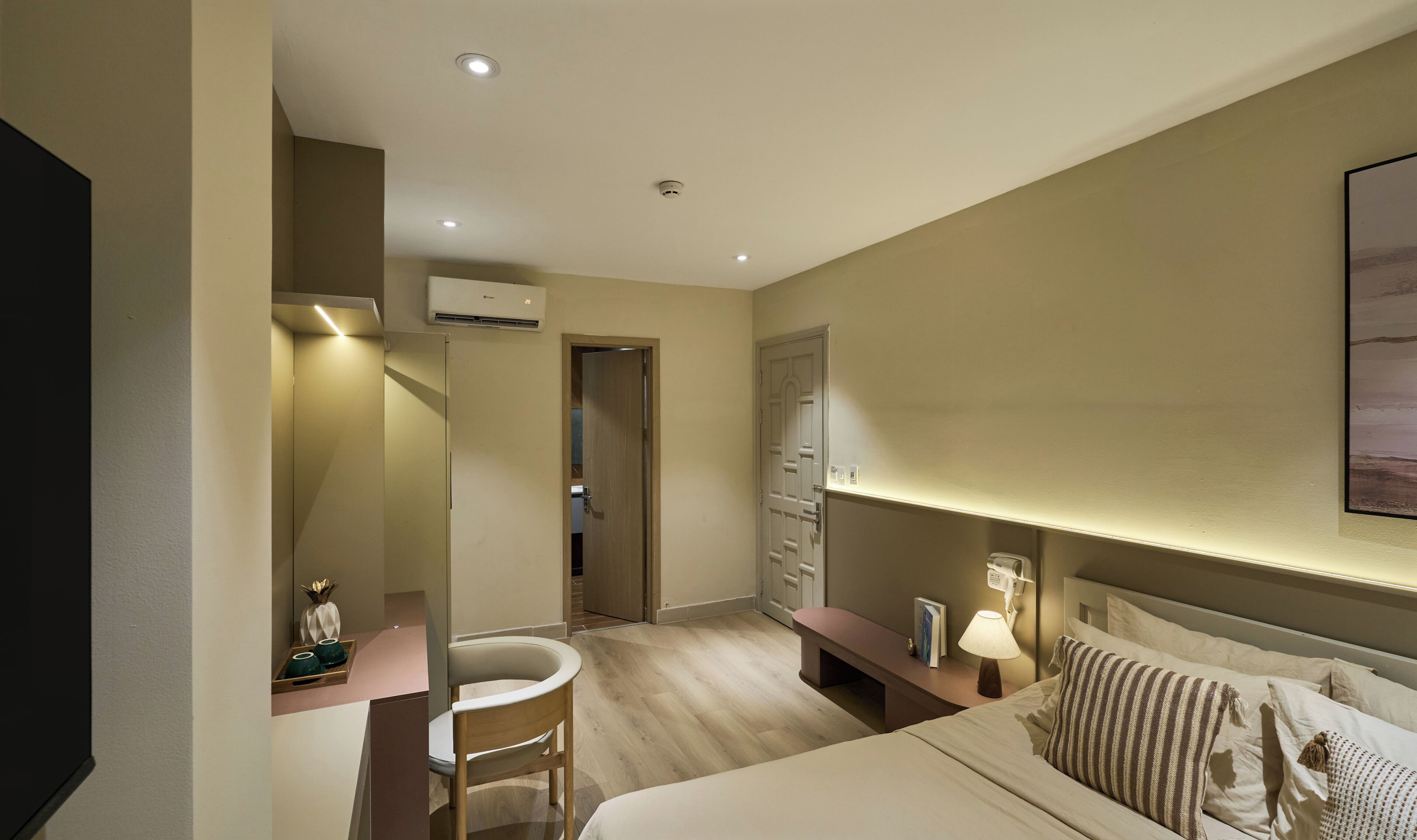 A hotel room with a bed, bedside table, lamp, and a painting on the wall.