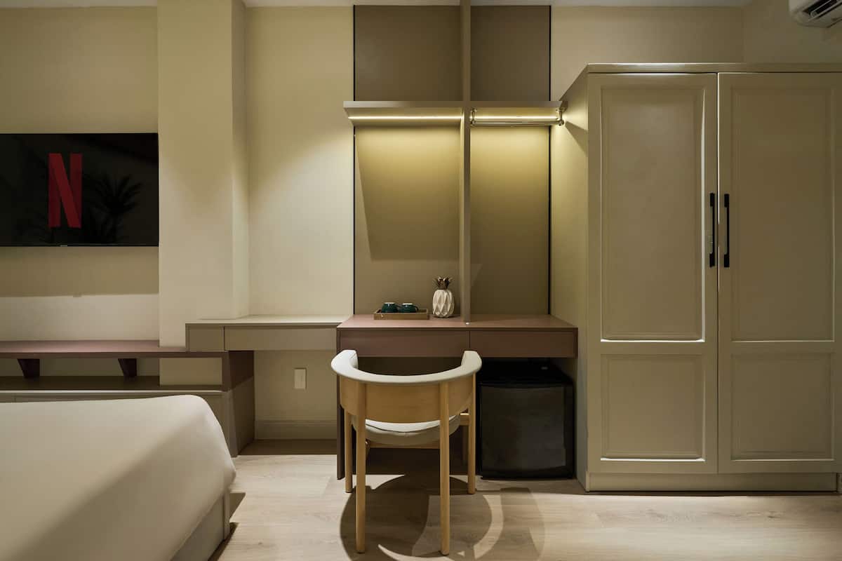 A bedroom with a bed, a desk, a chair, a wardrobe, and a TV mounted on the wall.