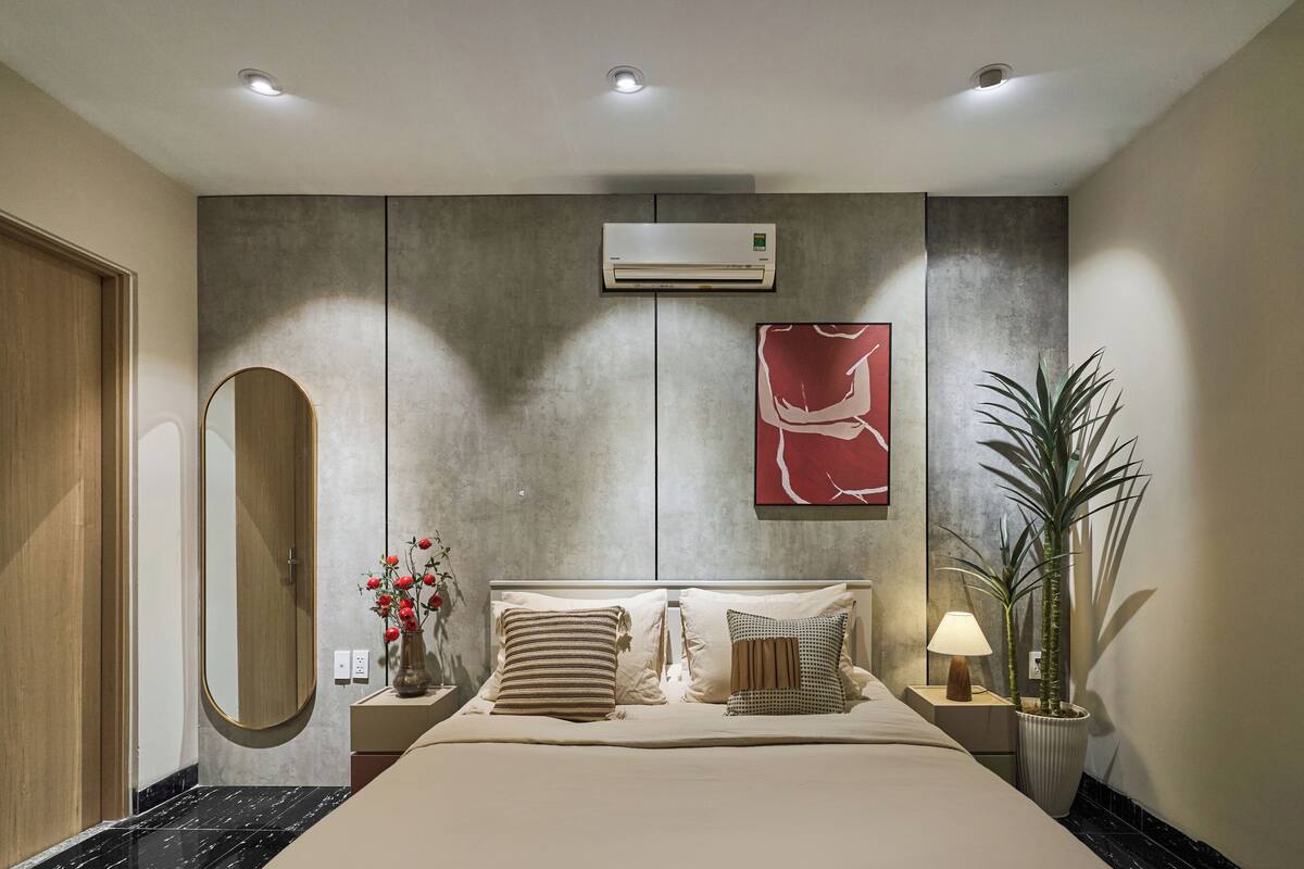 A modern bedroom with a bed, bedside tables, a mirror, an air conditioner, and a potted plant.