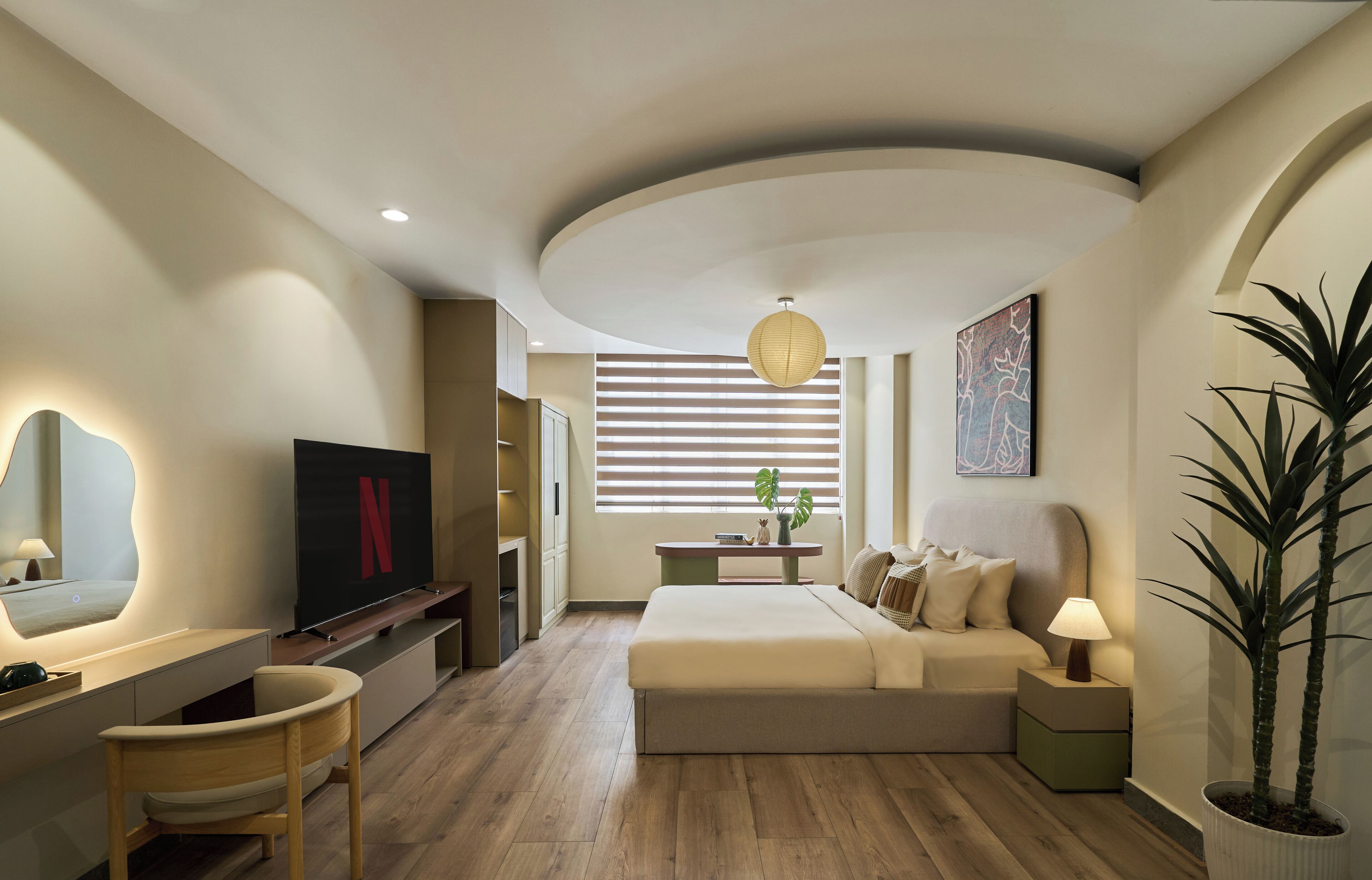 A modern bedroom with a bed, bedside table, lamp, TV, and a large potted plant.