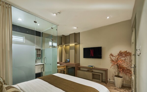 Habitación de hotel con cama, escritorio, espejo, televisor y planta en maceta.