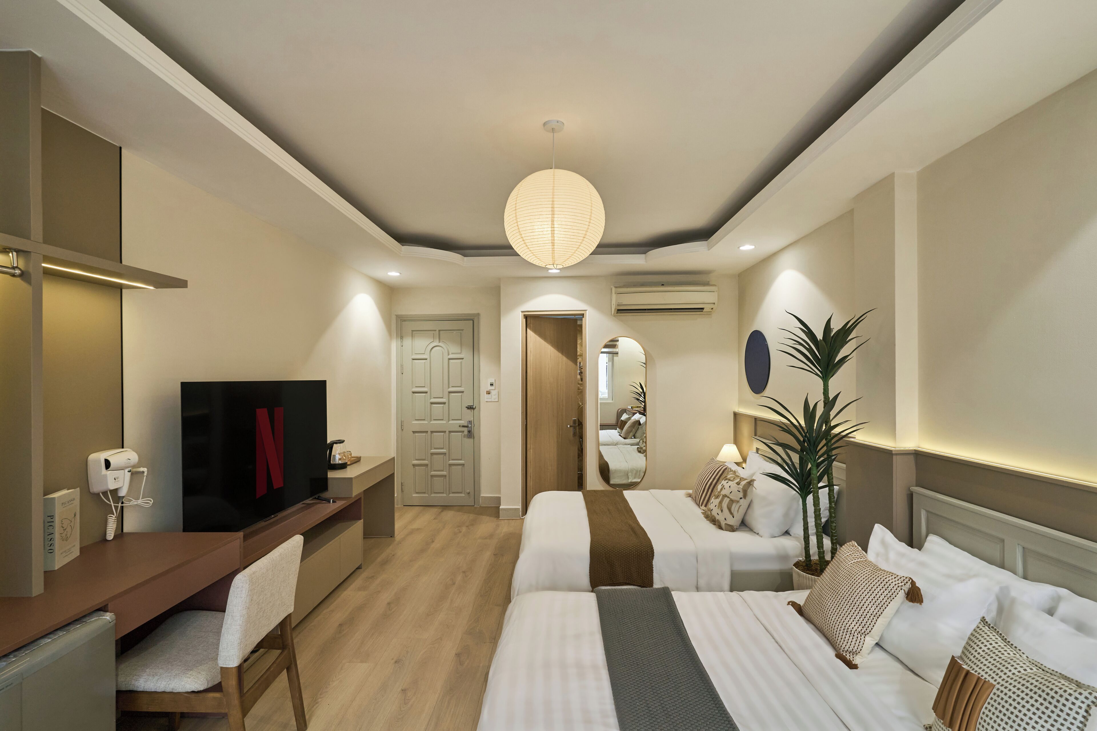 A hotel room with a TV, desk, two beds, a mirror, and a ceiling light.