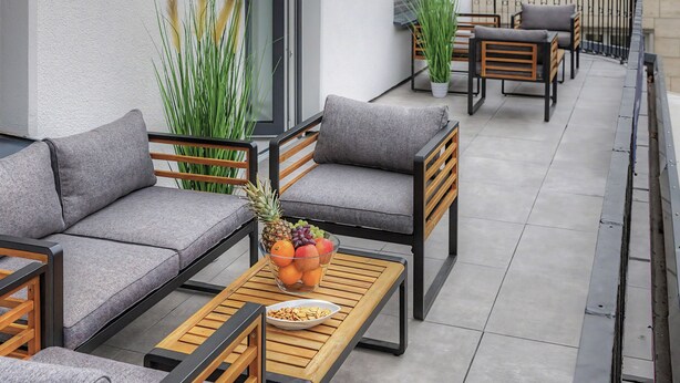 Een balkon met buitenmeubilair, een tafel met fruit en lekkernijen, en bloempotten.