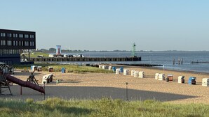 Een strand met strandhutten, een speeltuin, een pier en een gebouw op de achtergrond.