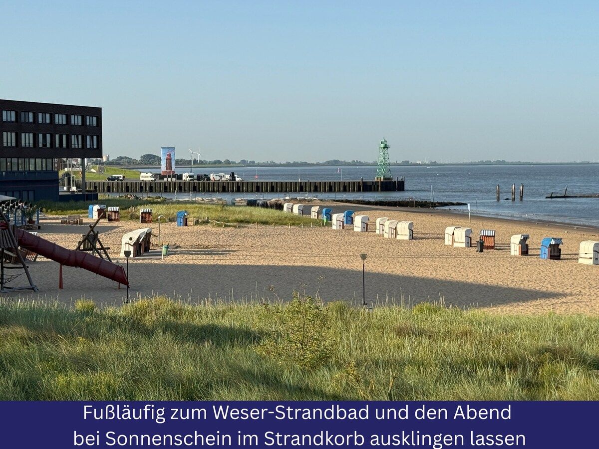Une plage équipée de toilettes mobiles, une jetée et un bâtiment visible au loin.