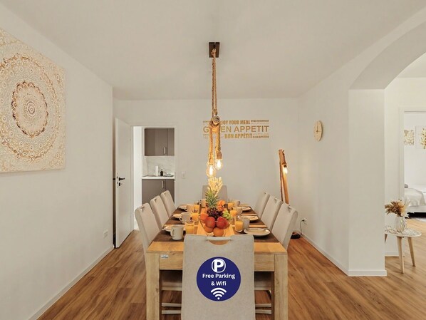 A dining area with a wooden table, chairs, and a fruit centerpiece. - Master’s Bridge: with garage & balcony near dyke (Bremerhaven)