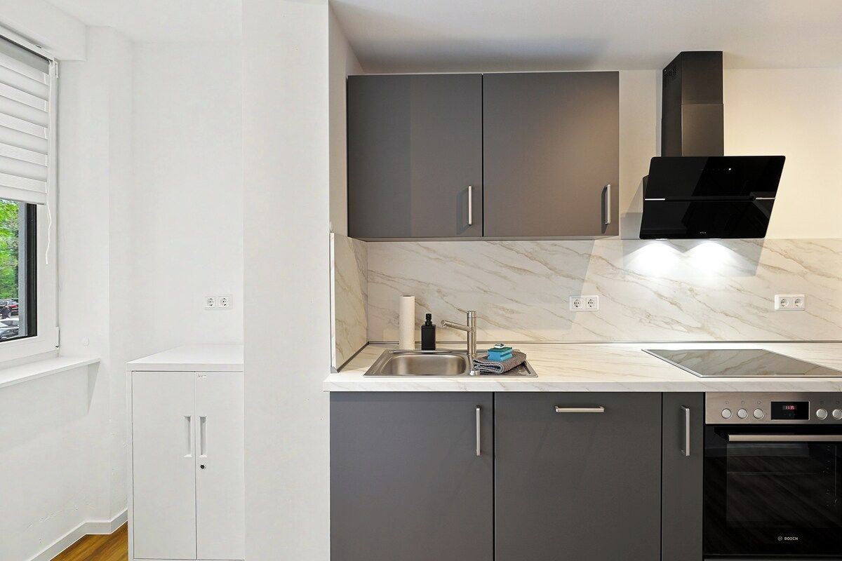A modern kitchen with grey cabinets, a Bosch oven, and a marble countertop.