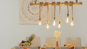 Een eethoek met een houten tafel, vier stoelen, een hanglamp met lampen en een decoratief wandobject.
