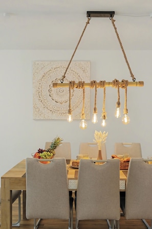 A dining area with a wooden table, four chairs, a hanging light fixture with bulbs, and a decorative wall piece. - Master's Bridge - Stylish, large balcony, close to the dike, 2 parking spaces, 2 WCs (Bremerhaven)