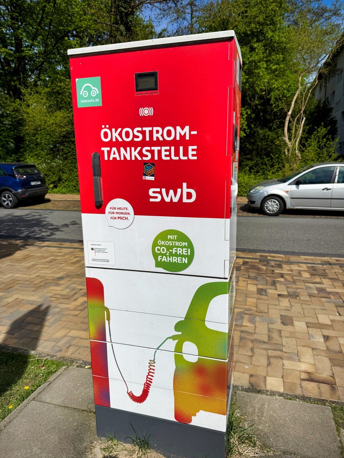 A red and white electric vehicle charging station with a green logo and text indicating it's a swb station.