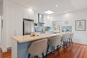 A modern kitchen with white cabinetry, a central island with bar stools, a stainless steel refrigerator, and a microwave.