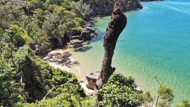 Un paysage côtier caractérisé par une formation rocheuse imposante, des eaux turquoise limpides et une végétation luxuriante.