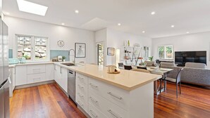 Une cuisine moderne avec des meubles blancs, un îlot central et un coin repas équipé d’un téléviseur et d’un canapé.
