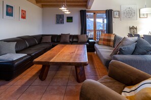 A living room with a wooden table, two sofas, and a balcony with a view. - Chalet With Sauna and Alpine Panoramas (Landry)
