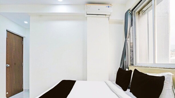 Ein Hotelzimmer mit einem Bett, einem Fenster mit Vorhängen, einer Klimaanlage und einer Holztür.