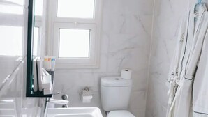 Een badkamer met een wit wastafel, toilet en bad. Er is een raam boven het toilet en een handdoekhouder aan de muur.