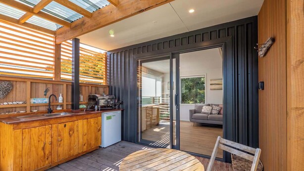 Une terrasse en bois dotée d’un bar intégré, d’une table ronde et d’une porte-fenêtre coulissante donnant sur un espace de détente extérieur.