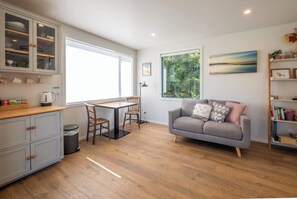 A modern kitchen with a dining table and chairs, a grey sofa, and a bookshelf.