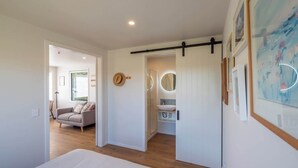 Une chambre moderne avec un grand lit, un canapé dans le salon attenant et une salle de bain équipée d’un lavabo et d’un miroir.