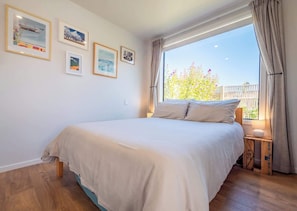 A bedroom with a large bed, a window with curtains, and several framed pictures on the wall.