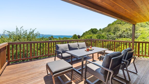 A wooden deck with a table and chairs, overlooking a scenic view of hills and a body of water.