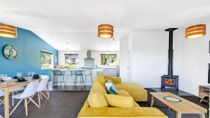 A modern living room with a yellow sofa, a dining area with a wooden table and chairs, and a kitchen in the background.