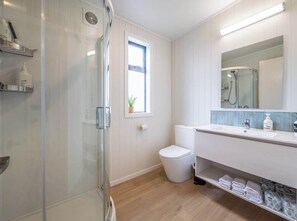 Une salle de bain moderne avec une douche à parois de verre, des toilettes, un lavabo avec un miroir et une fenêtre agrémentée d’une plante.