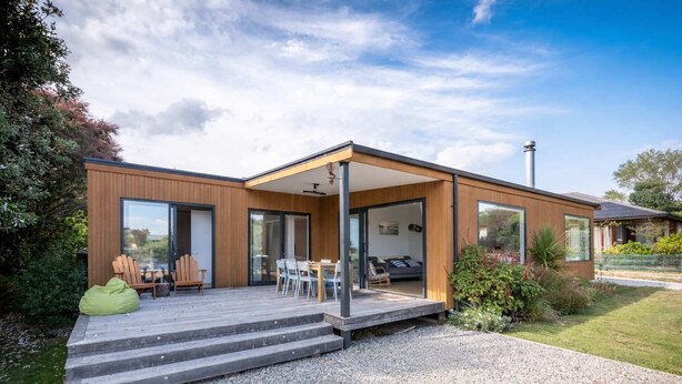 Ein modernes Haus mit überdachter Terrasse, Essbereich und sichtbarem Schlafzimmer.