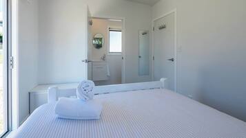 A bedroom with a large bed, a window, a bathroom with a mirror, and a door.