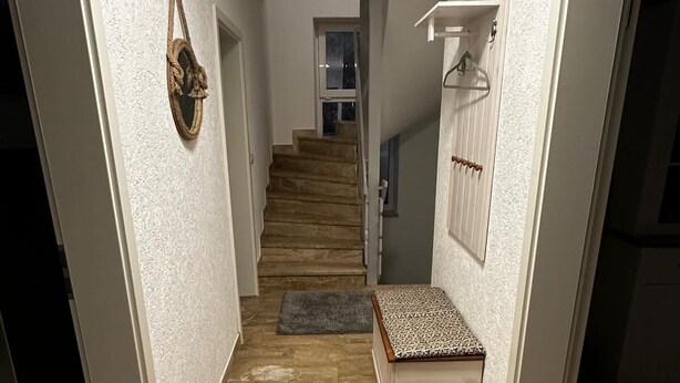 Un corridoio stretto con pavimento in legno, una panca con cuscino decorato e una scala che conduce a un piano superiore.