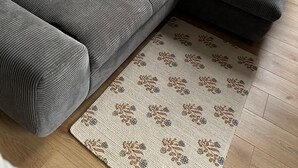 Un soggiorno moderno con un divano grigio, numerosi cuscini, un piccolo peluche e un tappeto decorato.