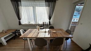 Zona pranzo con tavolo in legno, quattro sedie, una panca e una finestra con tende leggere.