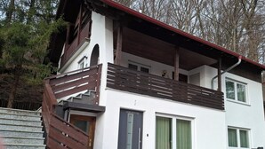 Un edificio su due piani con una scala in legno, un balcone e una porta con un numero.