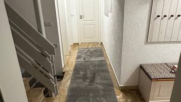 A hallway with a grey carpet, a white door at the end, and a white cabinet with hooks on the wall.