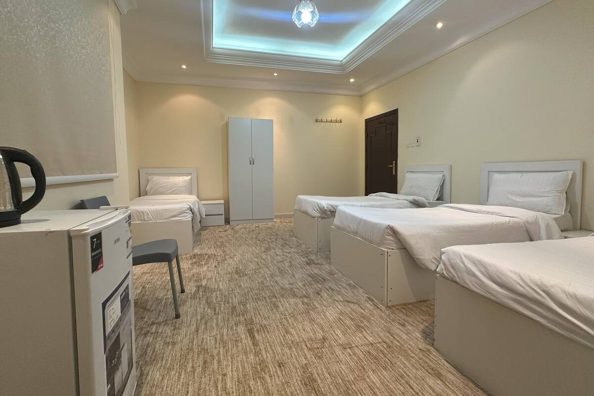 Habitación de hotel con dos camas, un armario, un escritorio con hervidor y una lámpara en el techo.