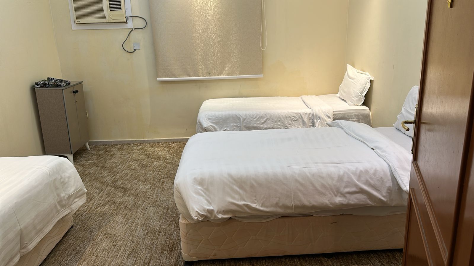 Una habitación de hotel con dos camas, un armario, un calentador y una ventana.