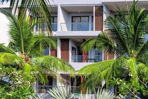 A modern multi-story building with balconies, surrounded by lush tropical vegetation.