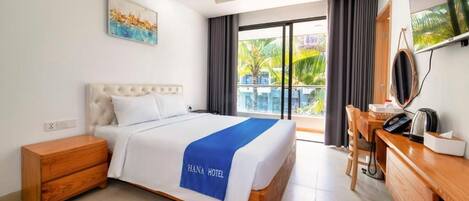 A hotel room with a bed, a desk, a chair, a TV, and a balcony with a view of palm trees.