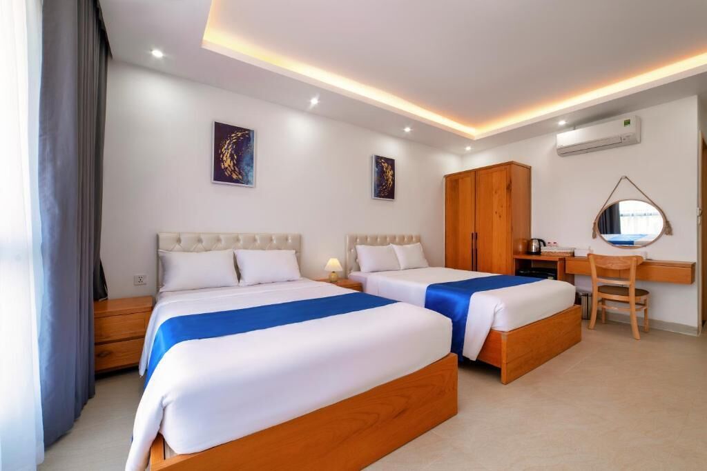 A hotel room with two beds, a desk, a chair, and artwork on the walls.