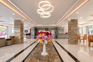 A modern lobby with a marble reception desk, a large floral centerpiece, and a chandelier.