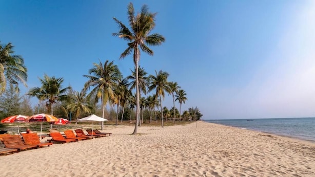 A beach with rows of wooden lounge chairs and umbrellas, palm trees, and a clear sky. - HANA HOTEL SONASEA NIGHT MARKET PHU QUOC (Phu Quoc)
