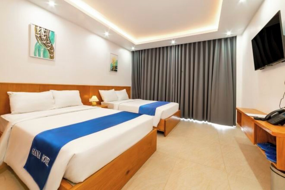 Ein Hotelzimmer mit zwei Betten, einem Schreibtisch mit Telefon und einem an der Wand befestigten Fernseher.